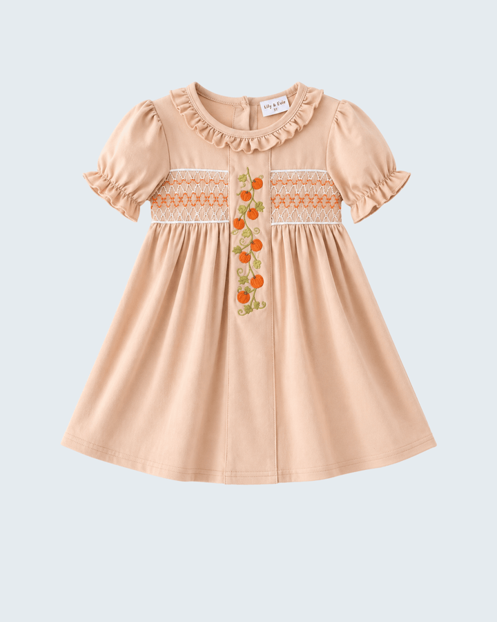 A peach-colored baby dress with short ruffled sleeves, a ruffled neckline, and smocked detailing across the chest with orange and green floral embroidery.
