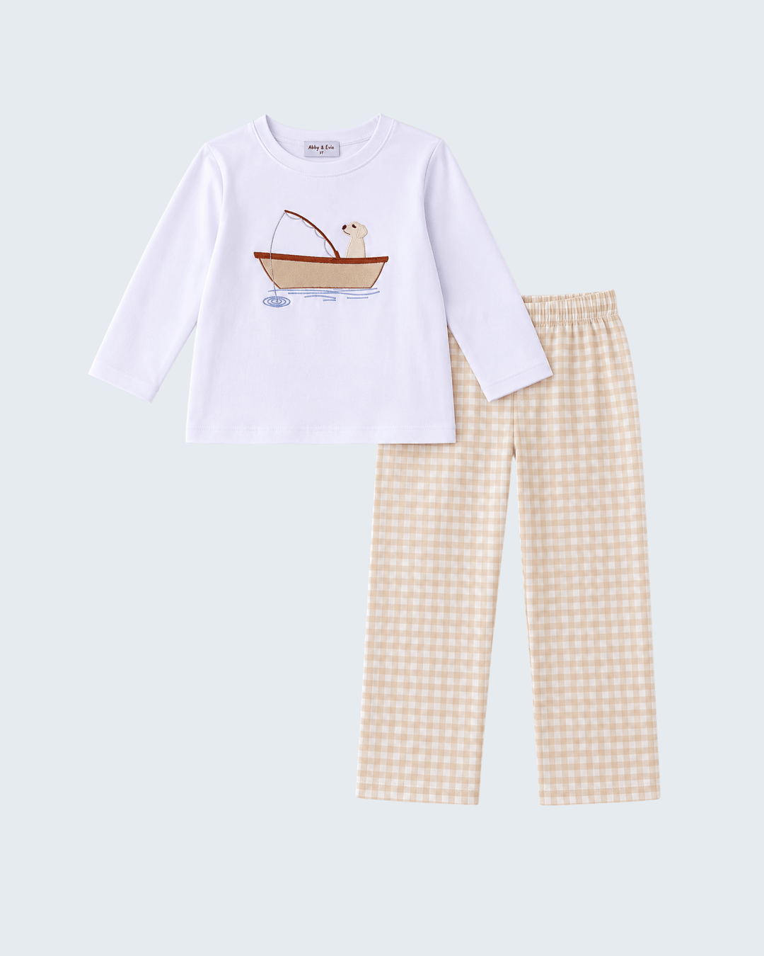 A children's two-piece pant set featuring a white long-sleeve top with a cartoon dog in a boat graphic on the chest, paired with beige and white gingham check pajama pants, shown on a light gray background.