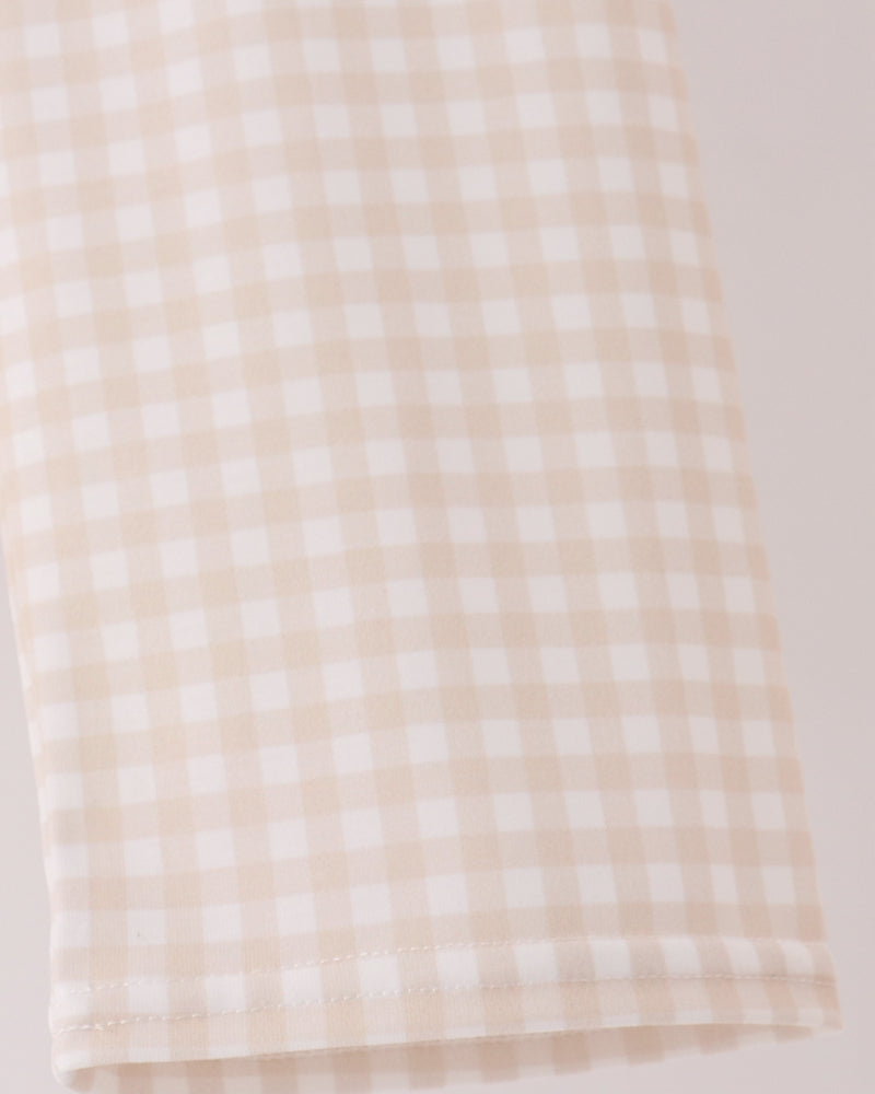 A close-up of a beige and white gingham checkered fabric, showing the fine woven pattern and folded hem.