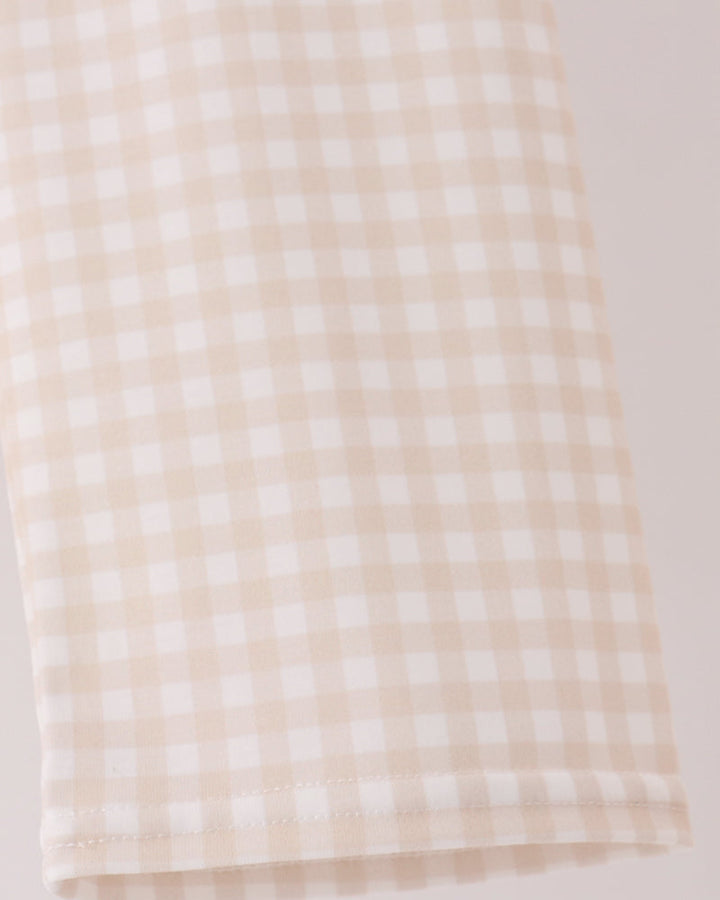 A close-up of a beige and white gingham checkered fabric, showing the fine woven pattern and folded hem.