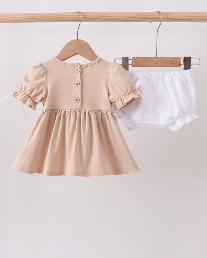 Beige dress and white shorts on hangers against a light gray background