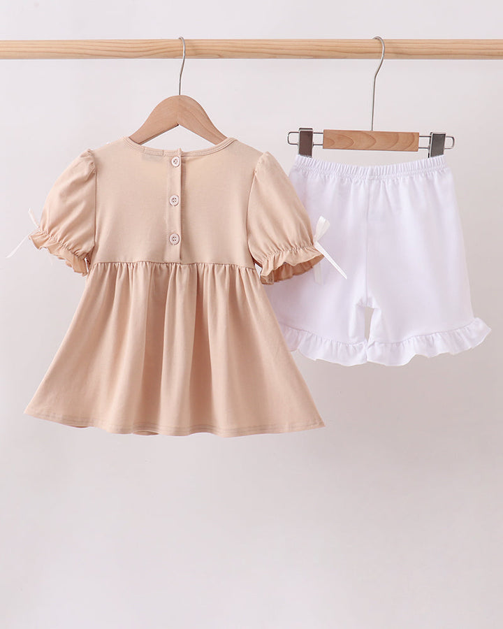 Beige dress with puff sleeves and white shorts on a wooden hanger against a beige background