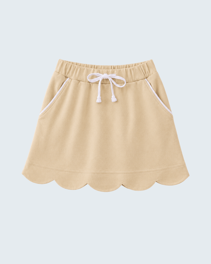 A light beige mini skirt with a scalloped hem, white drawstring waist, and white piping details on the side pockets, shown against a light gray background.