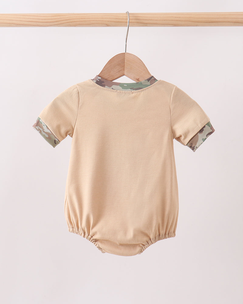 Beige baby romper with green trim on a wooden hanger against a white background