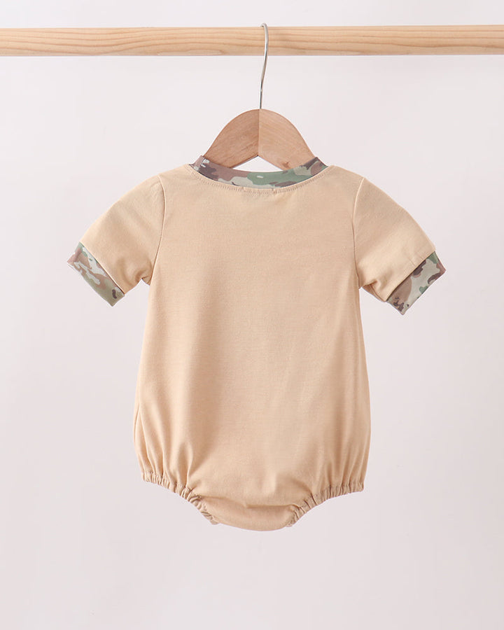 Beige baby romper with green trim on a wooden hanger against a white background