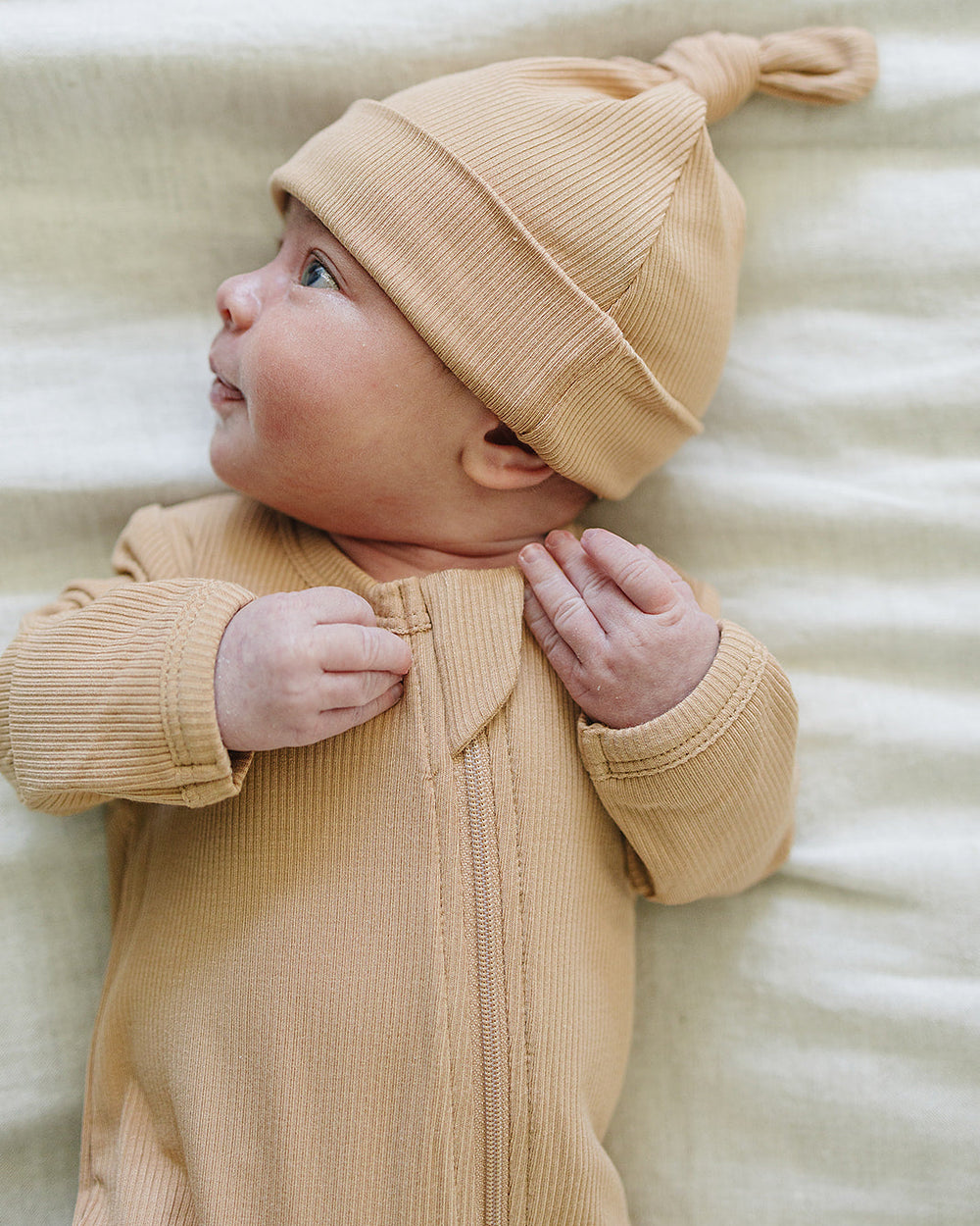 Baby wearing a yellow outfit and hat lying on a textured surface