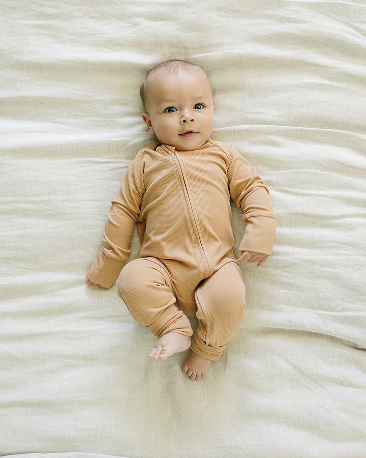 Baby in a beige onesie lying on a white blanket