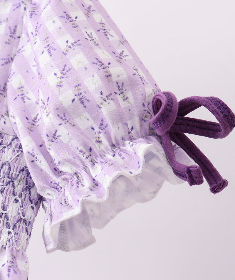 Close-up of a purple floral dress with ruffled details on a light gray background