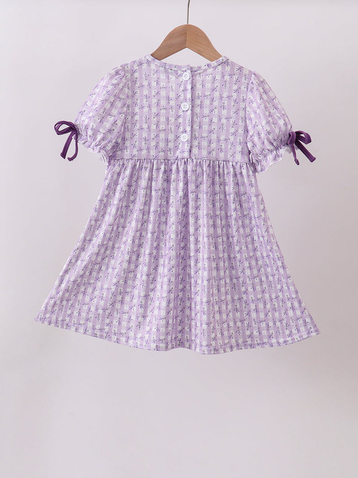 Purple checkered dress with bow sleeves on a hanger against a white background
