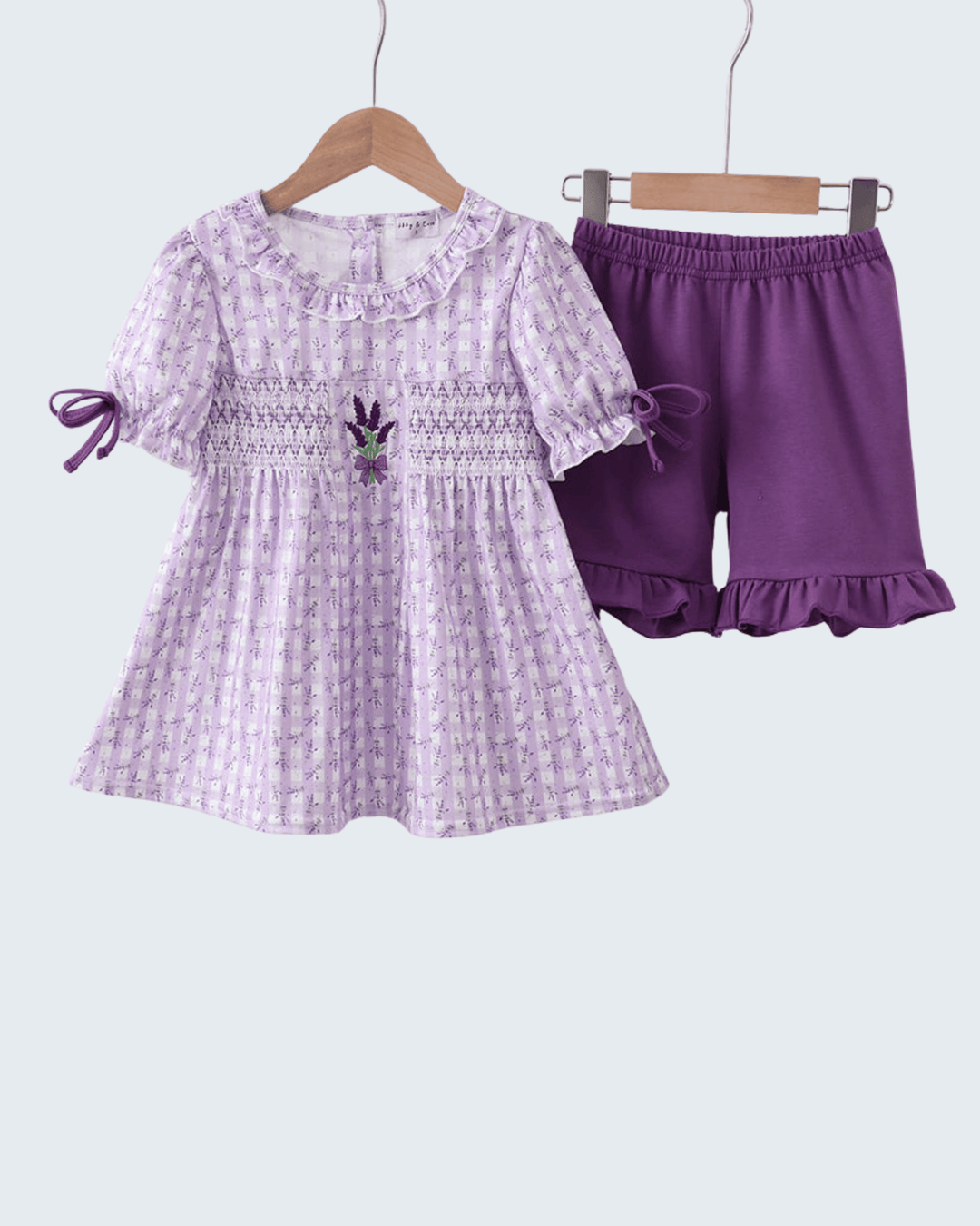 Purple dress with floral pattern and matching shorts on hangers against a white background