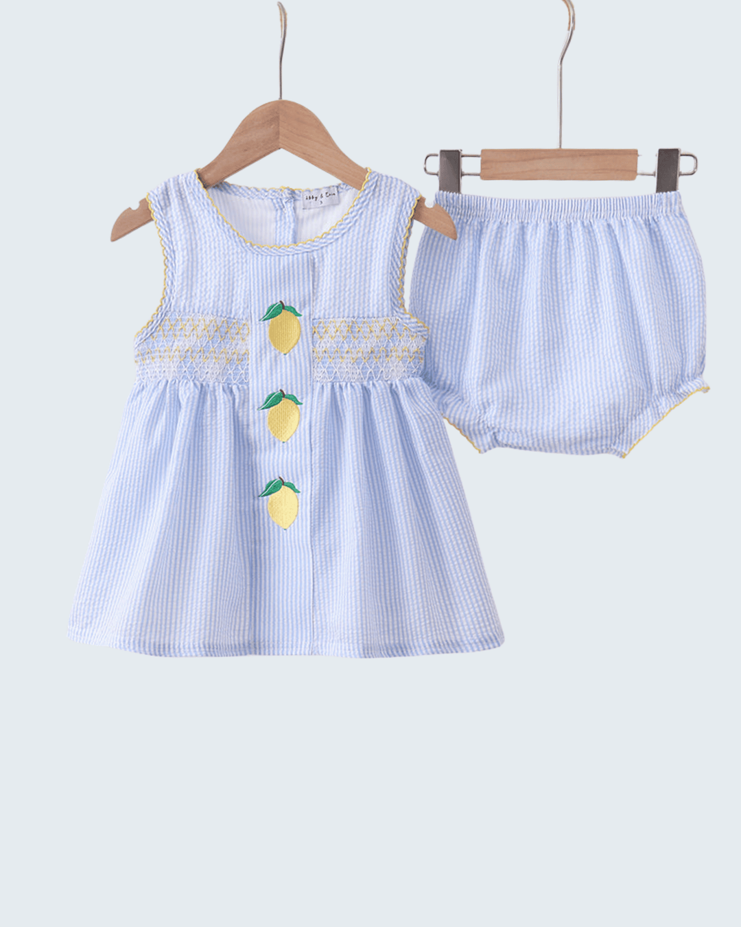 Children's blue striped dress with lemon designs on a hanger against a light gray background