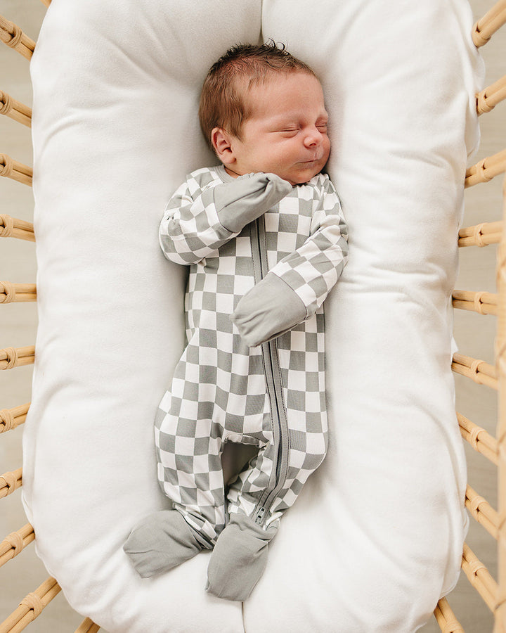 Newborn baby sleeping in a white crib with a checkered outfit