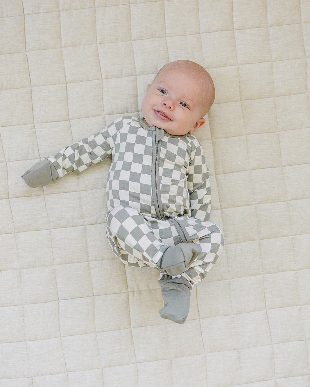 Baby wearing a gray checkered onesie lying on a quilted surface