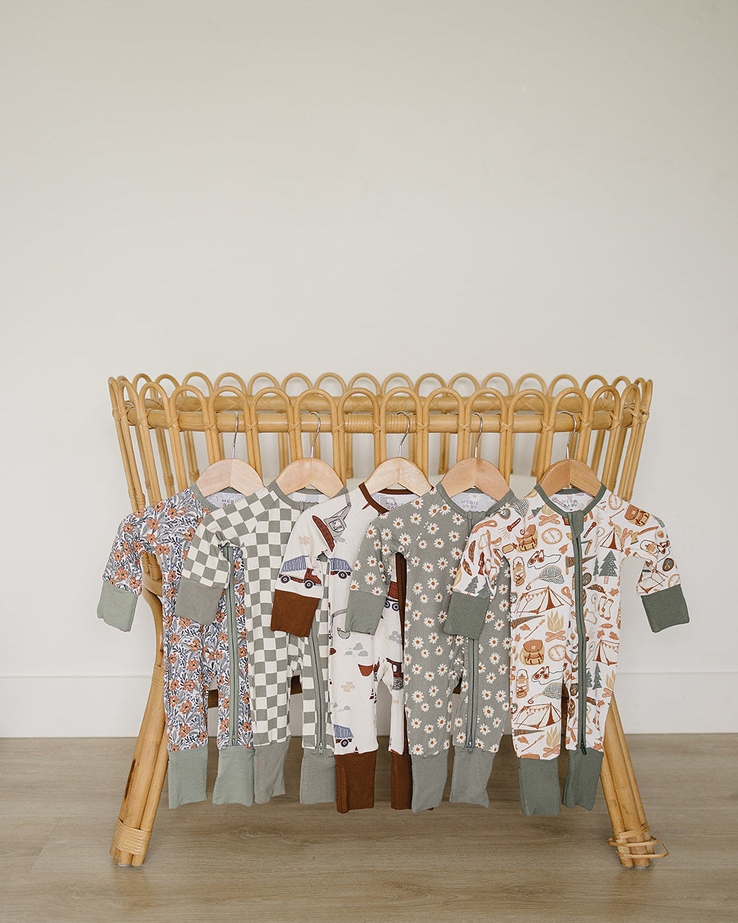 Collection of baby rompers on a wooden rack against a plain wall.