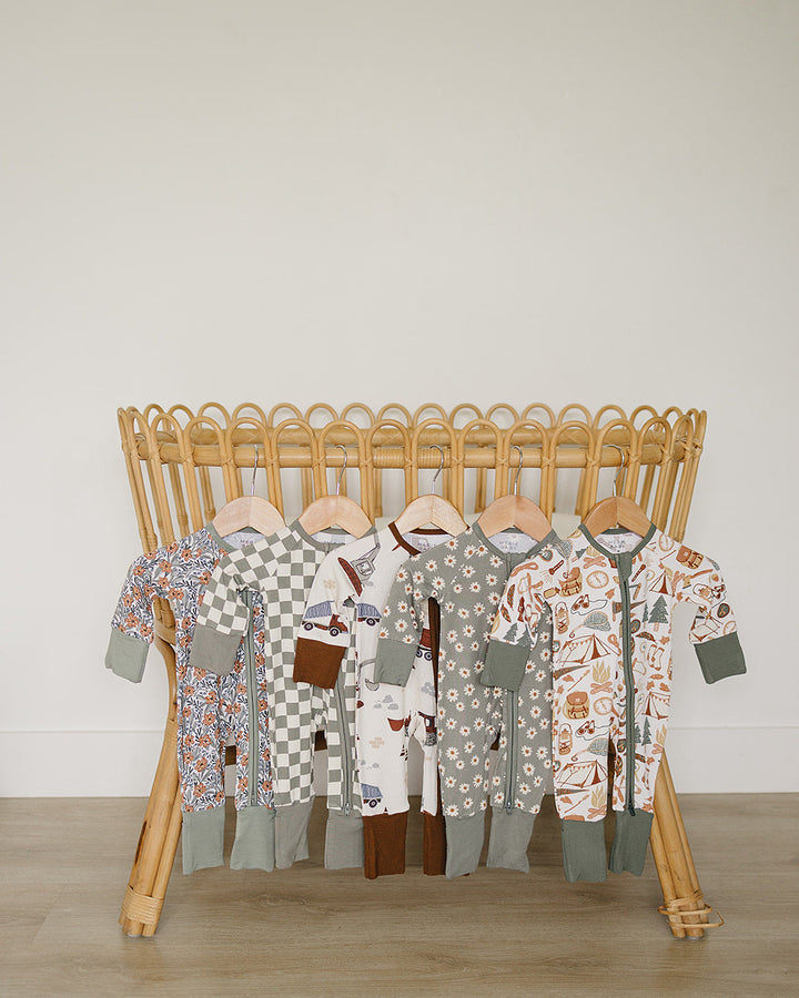 Collection of baby rompers on a wooden rack against a plain wall.