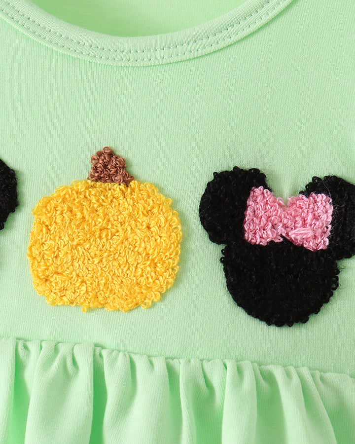 Close-up of a light mint green garment featuring a yellow textured pumpkin applique and a black Minnie Mouse-style mouse head applique with a pink bow.