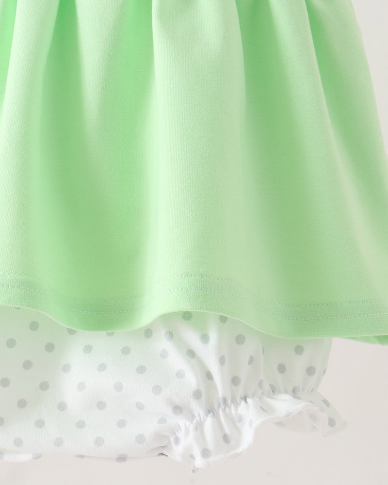 A close-up of a mint green skirt or dress hem layered over white ruffled bloomers with small gray polka dots, shown against a plain light background.