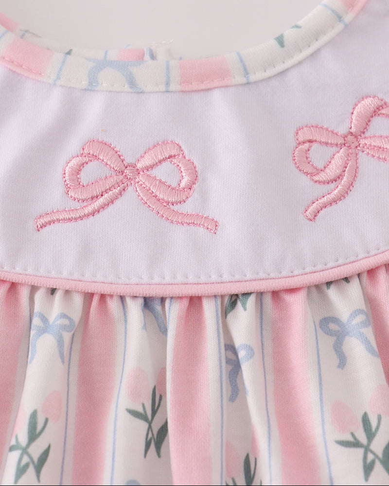 Close-up of a dress with pink bows and floral patterns on a light background