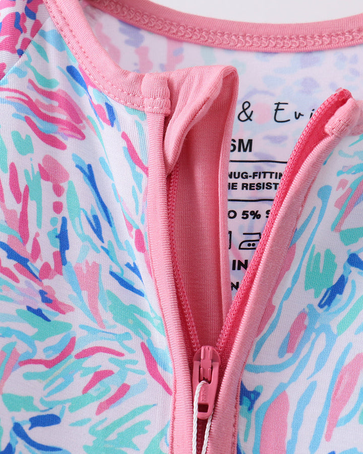 Close-up of a colorful swimsuit with a pink zipper on a multicolored abstract pattern background.
