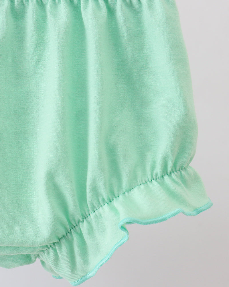 Light green baby bloomers with ruffled edge on a light gray background