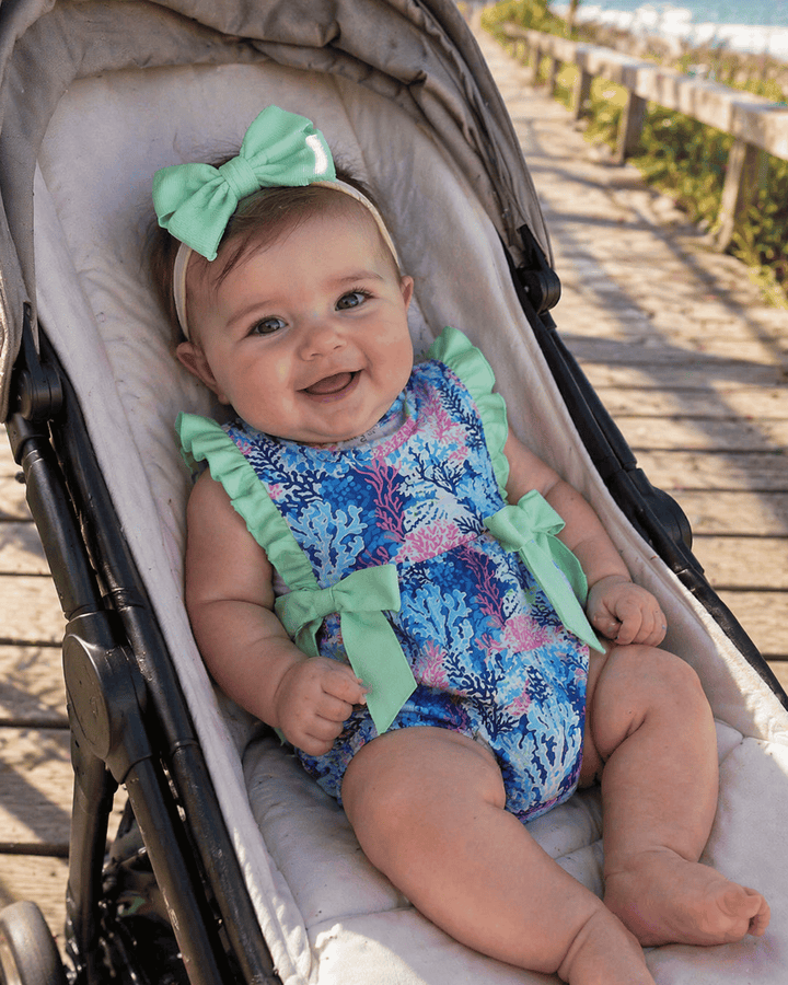 Baby in a colorful romper with green bows sitting in a stroller.