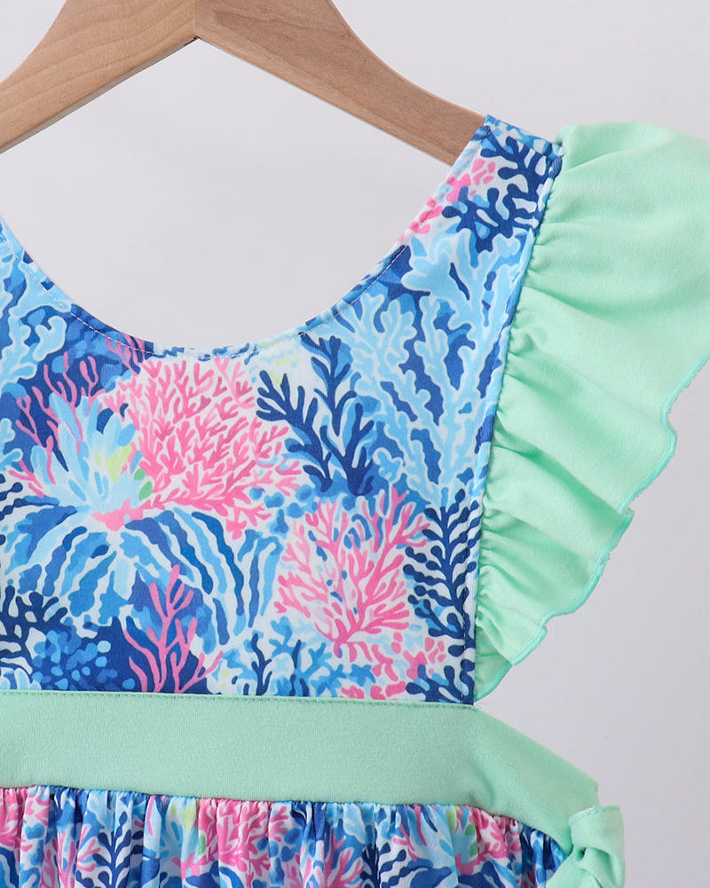 Dress with coral reef pattern and ruffled green trim on a hanger.