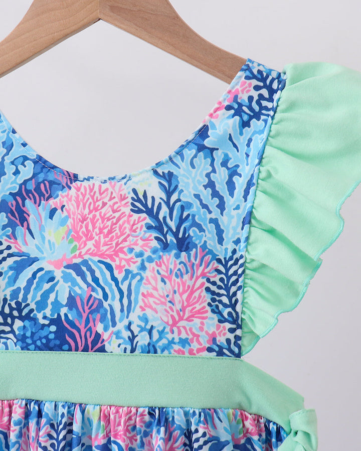 Dress with coral reef pattern and ruffled green trim on a hanger.