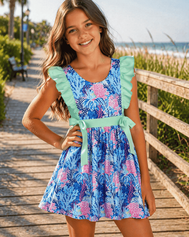 Young girl in a colorful dress standing on a wooden boardwalk by the beach.
