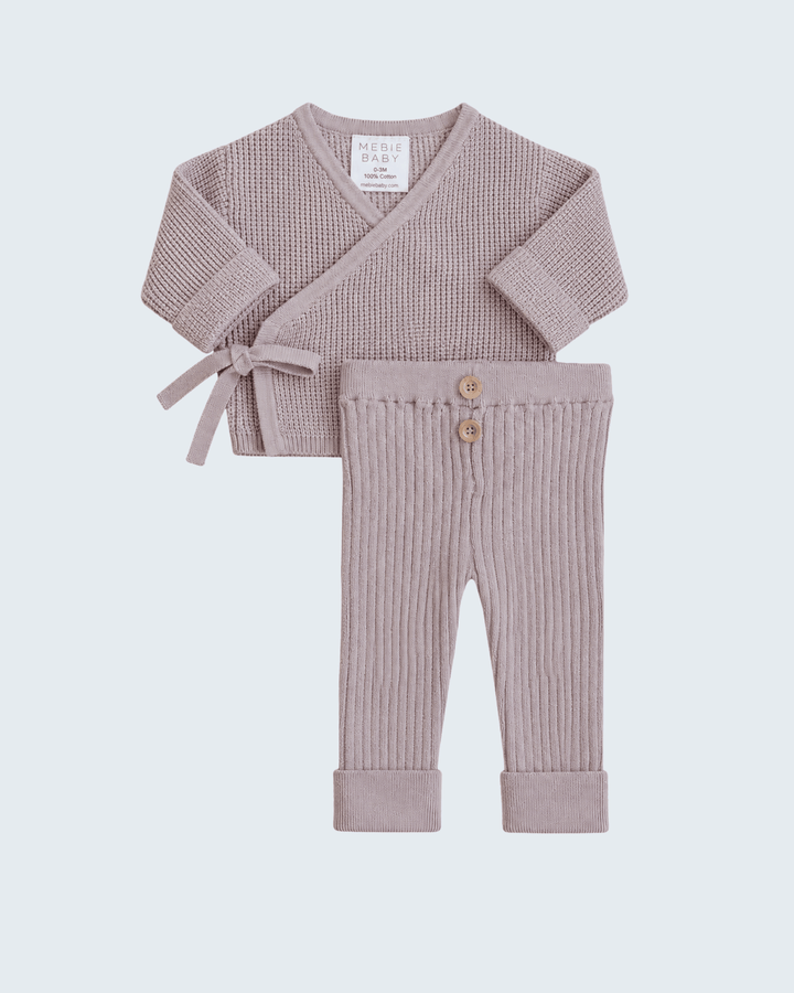 A baby knit two-piece set featuring a short-sleeve wrap-style top with a side bow and matching ribbed pants with button details, in a dusty mauve color.