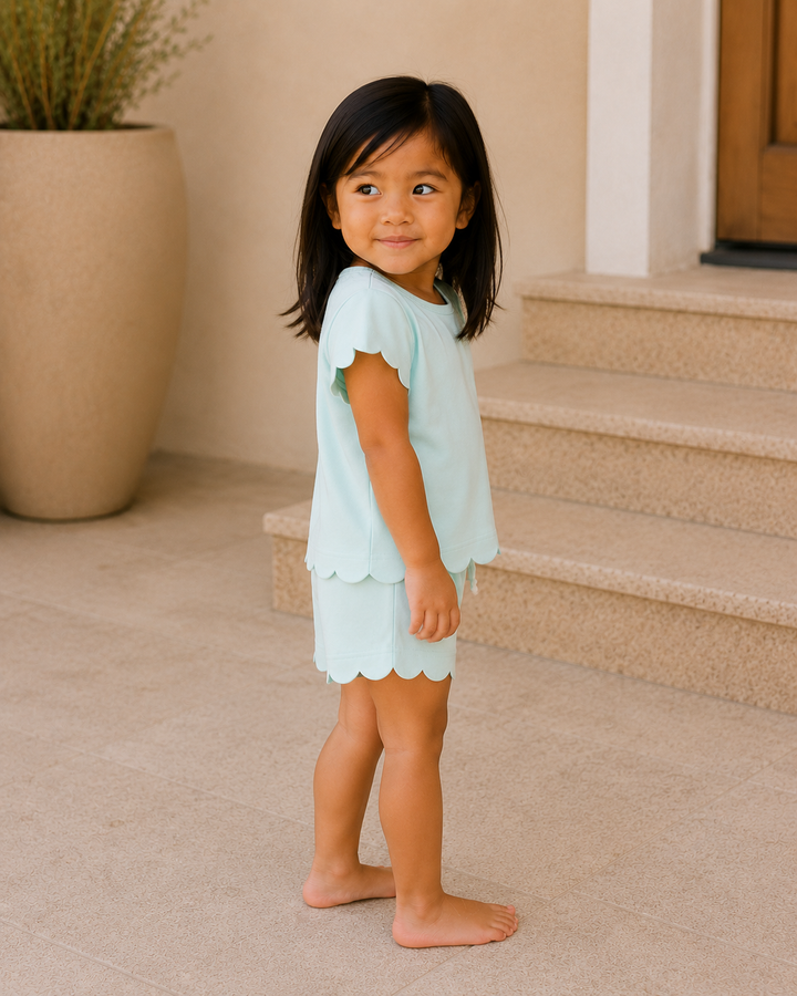 Young girl in a light blue outfit standing on a porch.