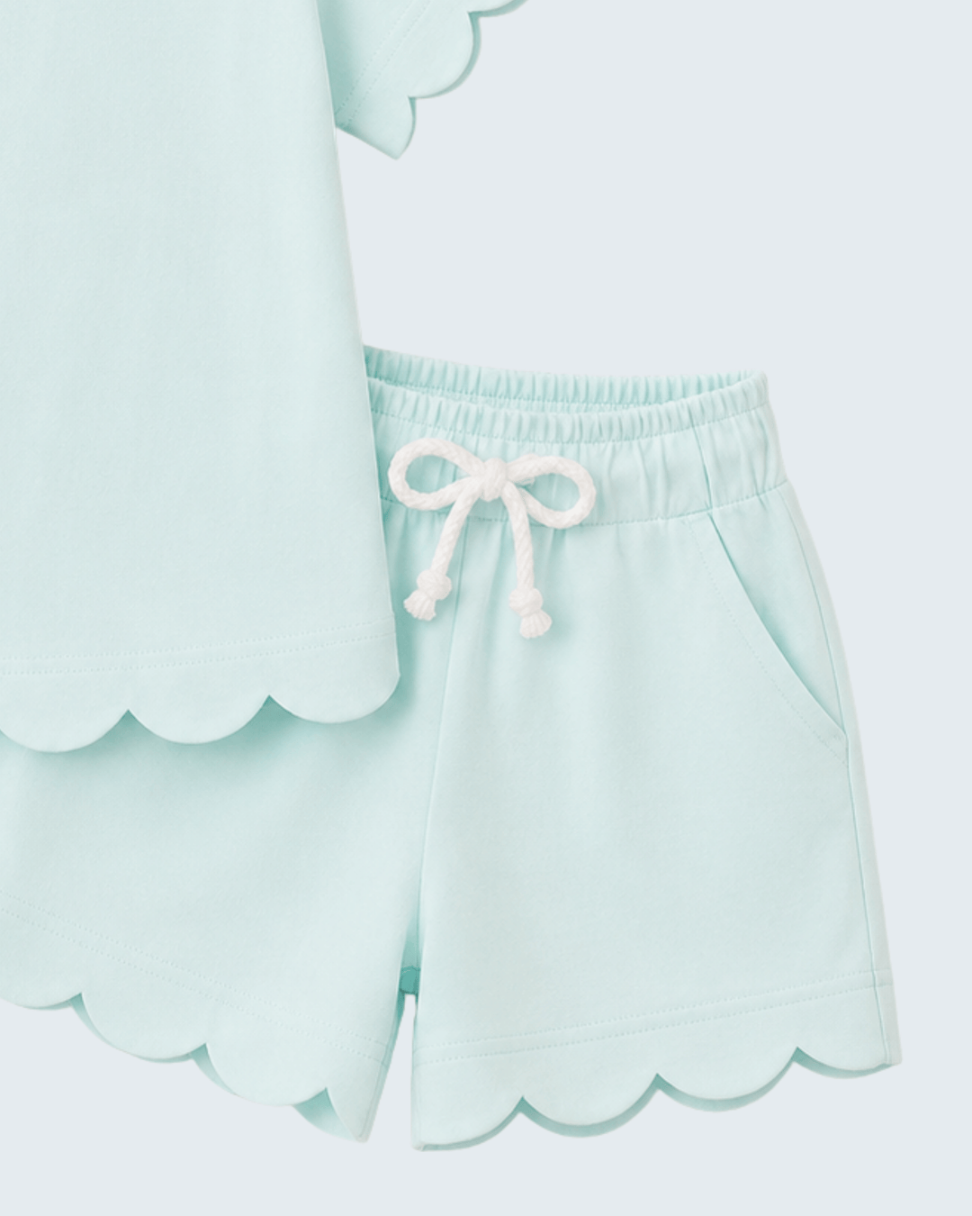 Light blue shorts with scalloped edges and a white drawstring on a light gray background