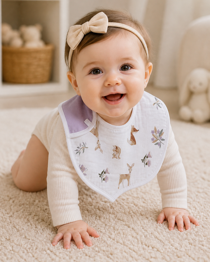 Baby wearing a bib with animal prints and a headband, sitting on a carpeted floor.