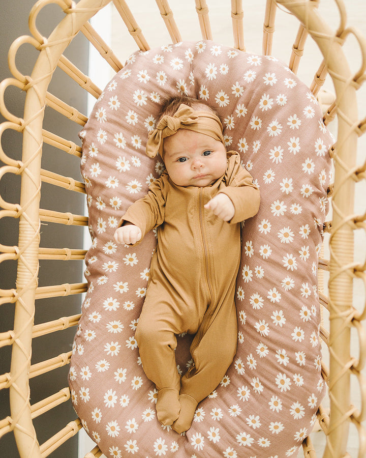 Baby in a yellow outfit lying on a floral-patterned cushion inside a wicker chair.