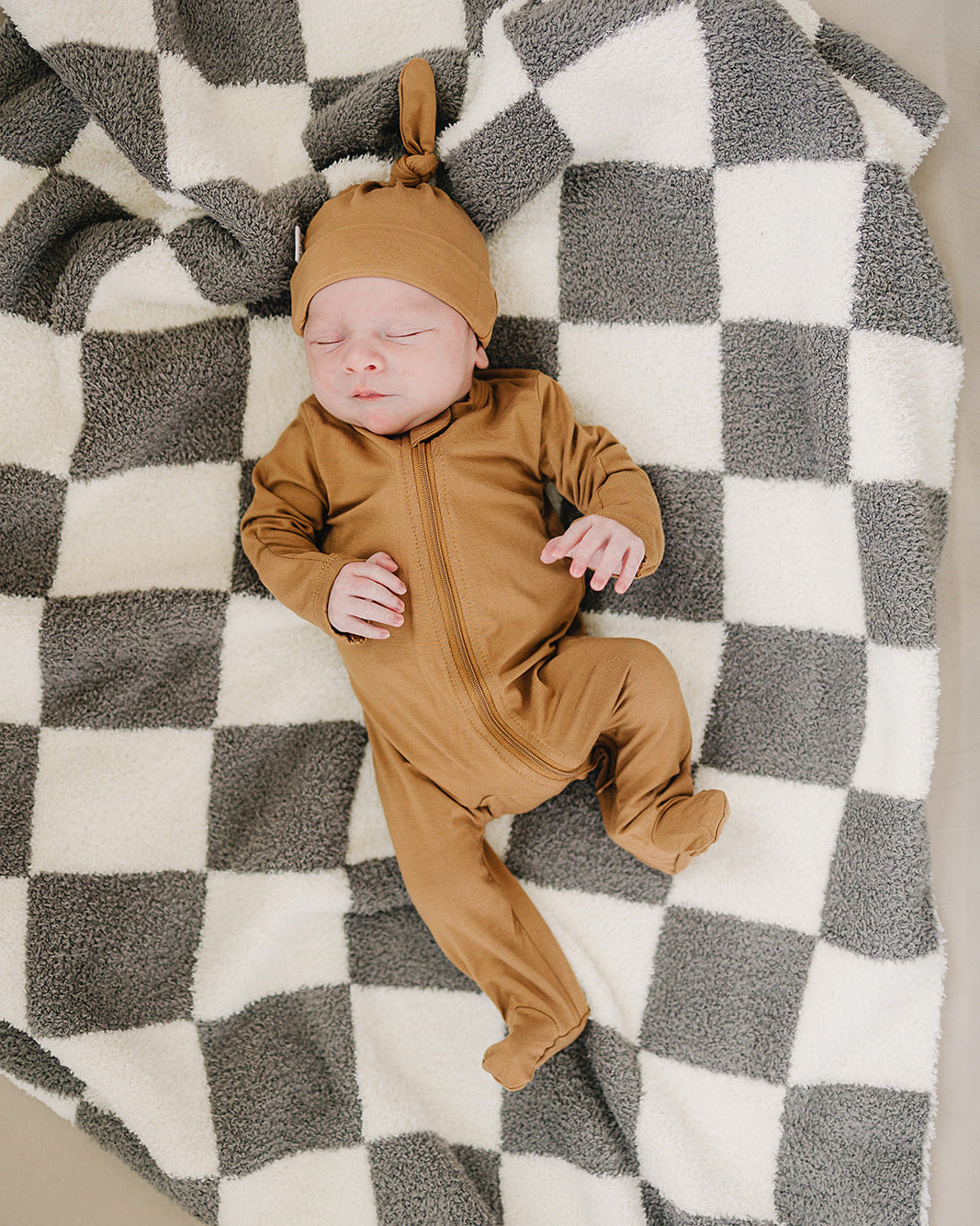 Baby in a brown outfit lying on a checkered blanket