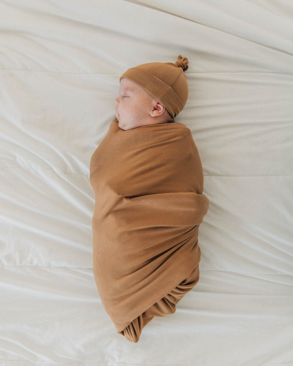 Tan baby knot hat and matching swaddle blanket in side pose