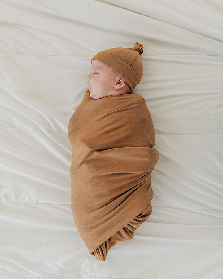 Tan baby knot hat and matching swaddle blanket in side pose