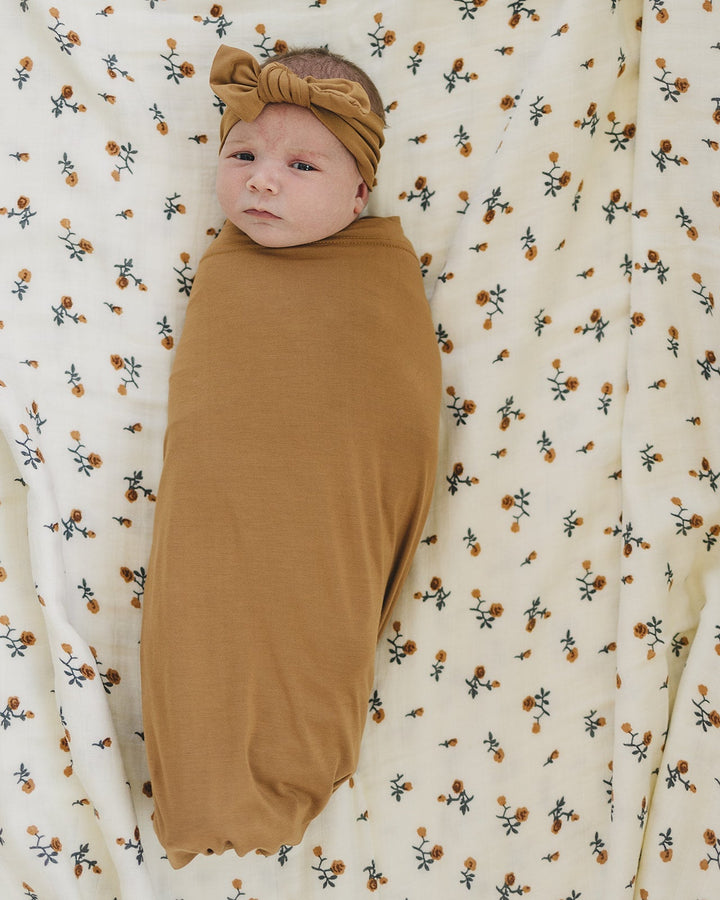 Tan baby head wrap and matching swaddle blanket on patterned bedding