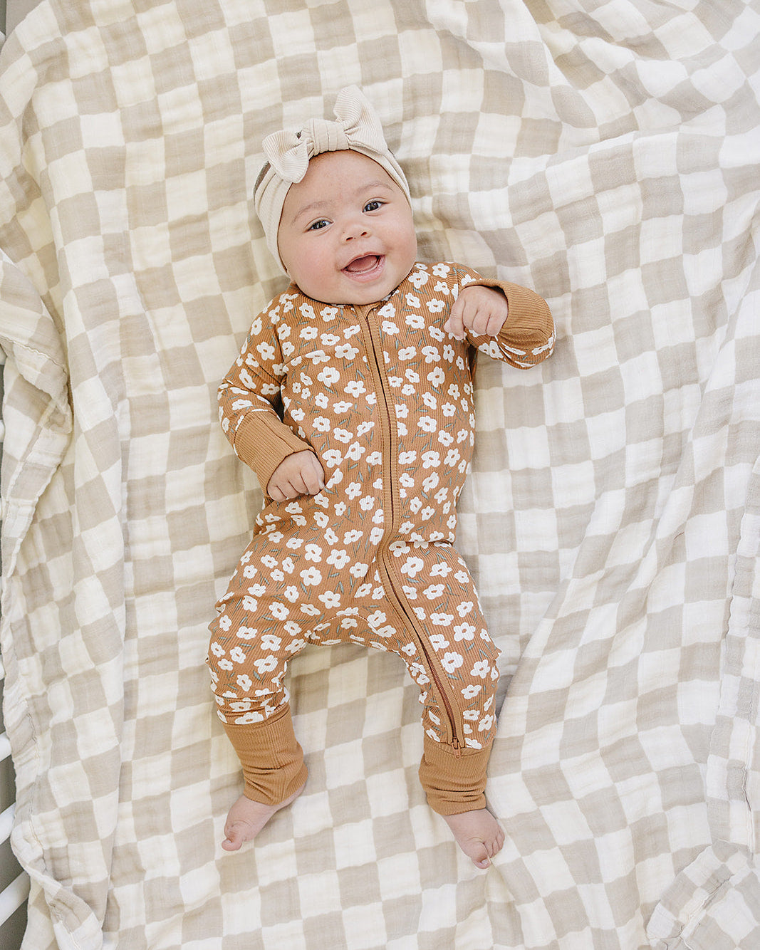 Baby in a floral onesie lying on a checkered blanket