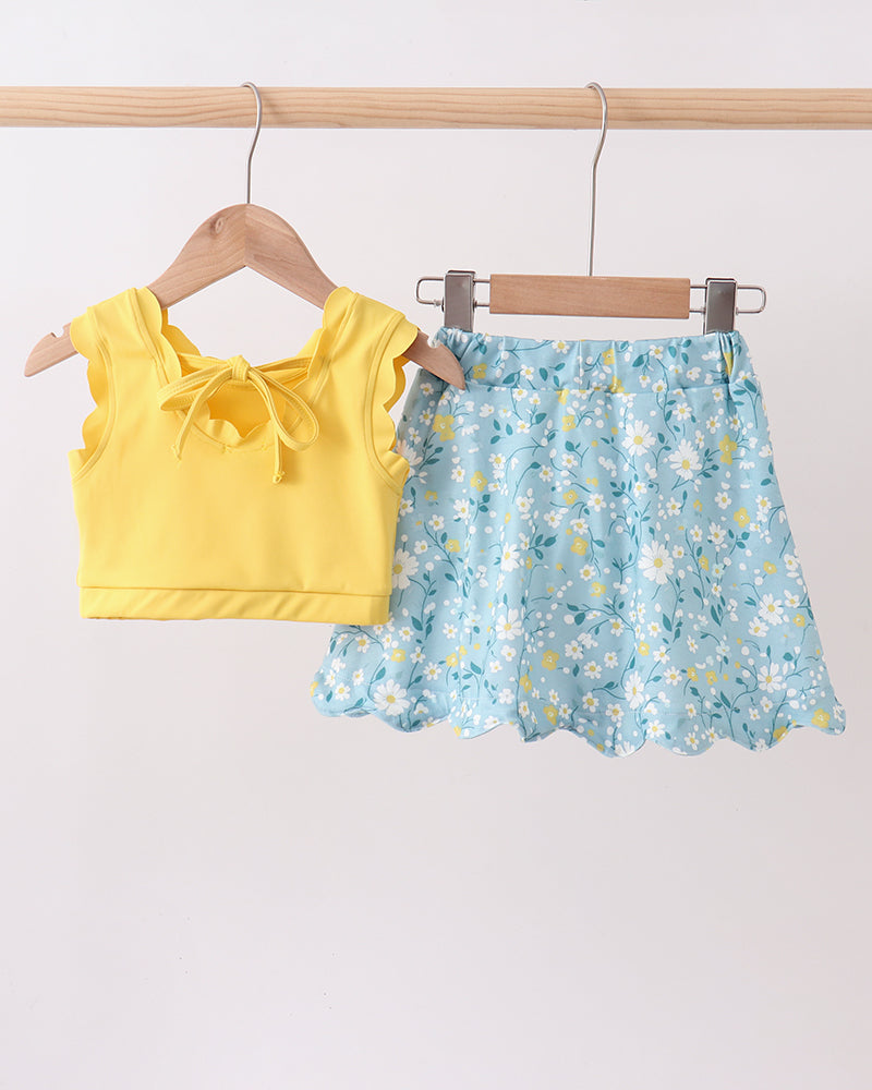 Yellow top and blue floral skirt hanging on wooden hangers against a white background