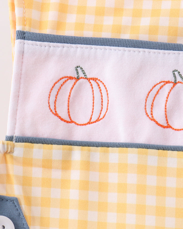 Close-up of a yellow and white gingham fabric item with a white band featuring embroidered orange pumpkins and gray trim.