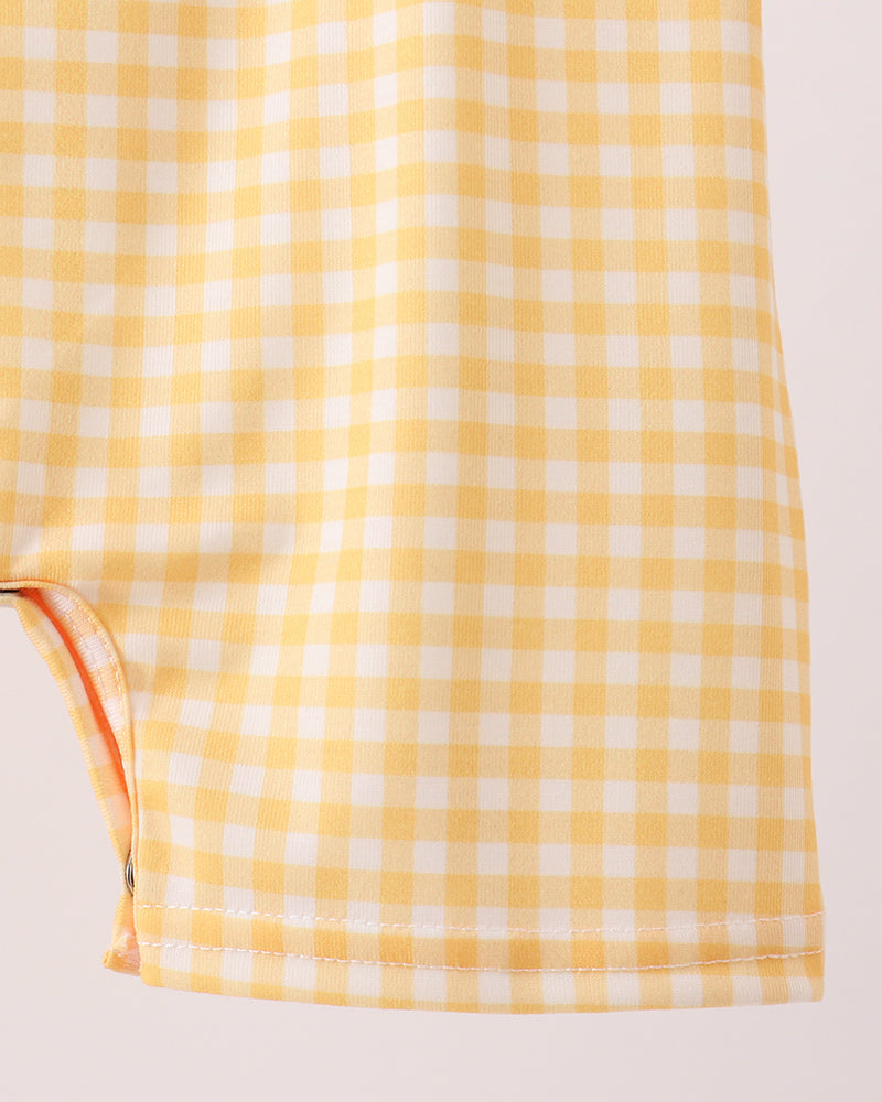 Close-up of a yellow and white gingham fabric item, showing the checkered pattern and stitched hem against a plain light background.