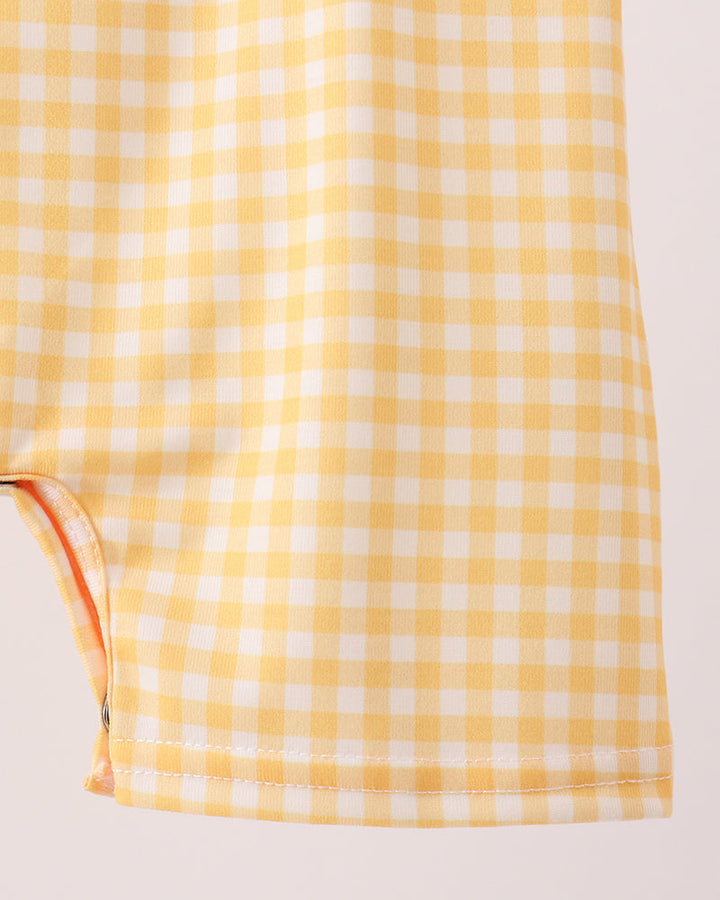 Close-up of a yellow and white gingham fabric item, showing the checkered pattern and stitched hem against a plain light background.