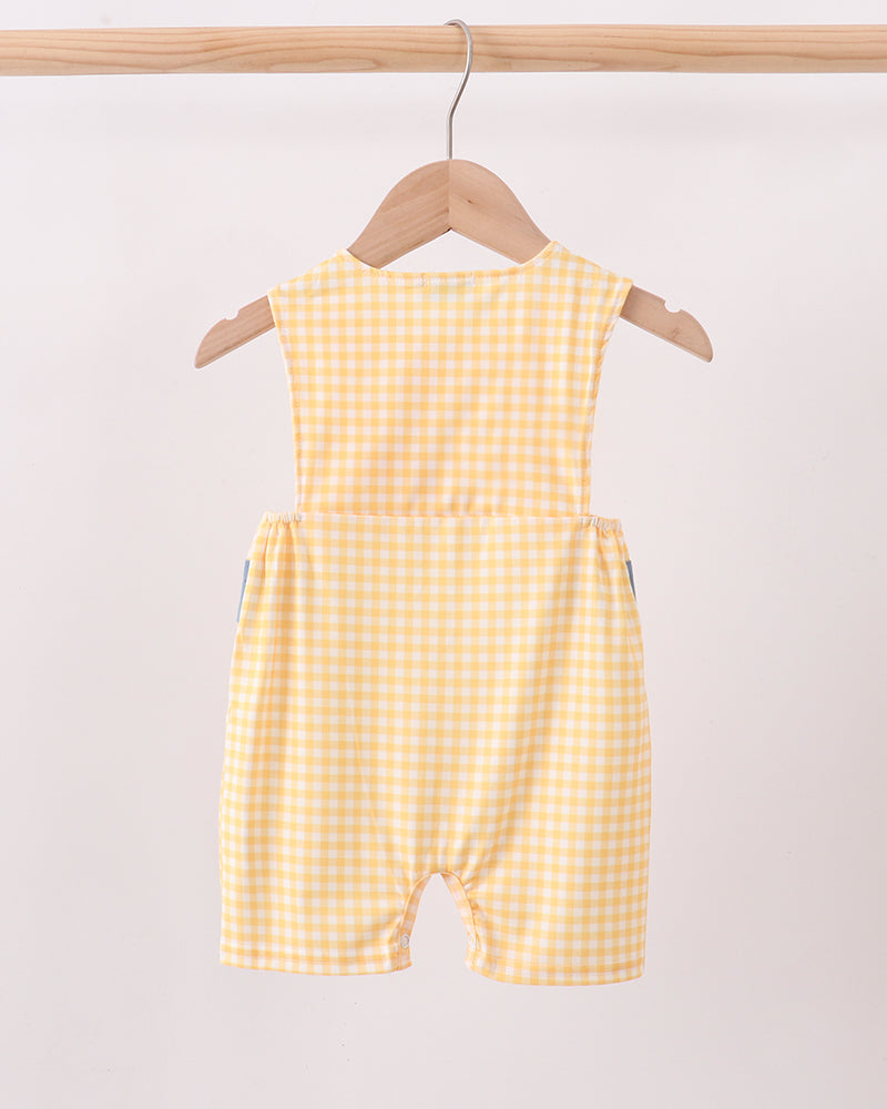 A yellow and white gingham baby romper hanging on a wooden hanger from a light wood clothing rack against a plain off-white background.