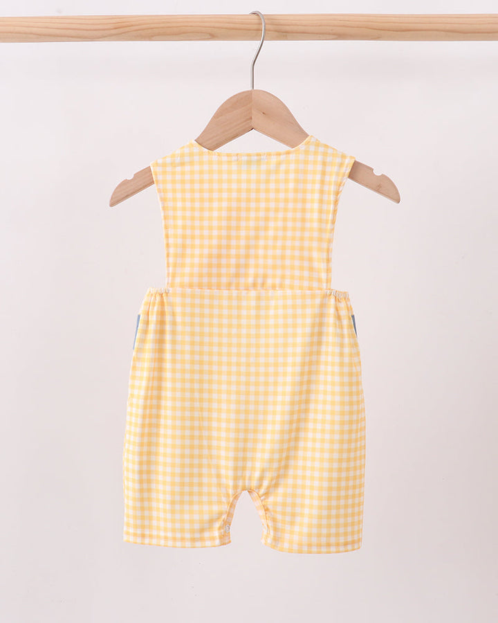 A yellow and white gingham baby romper hanging on a wooden hanger from a light wood clothing rack against a plain off-white background.