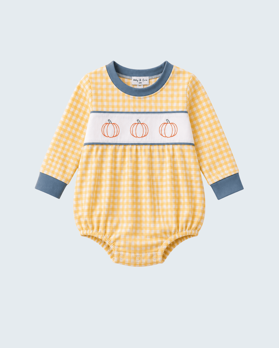 A baby long-sleeve romper in a yellow and white gingham pattern, featuring a white chest stripe with three orange pumpkin illustrations and blue-gray trim on the collar, cuffs, and hem.