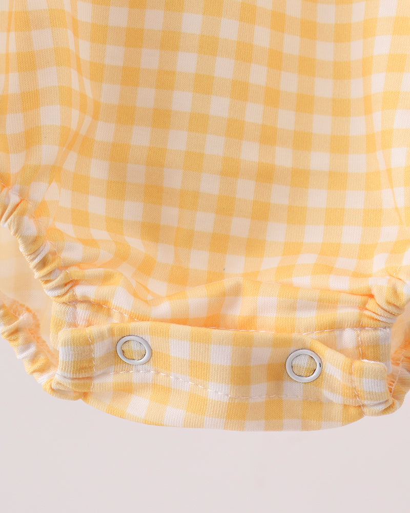 Close-up of a yellow and white gingham check fabric garment with a ruffled snap-closure hem, shown against a plain light background.