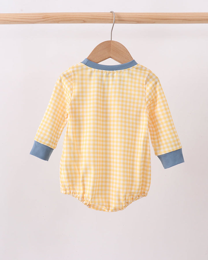 A baby long-sleeve romper in a yellow and white gingham check pattern, hanging on a wooden hanger from a wooden clothes rack. The romper features contrasting light blue ribbed trim at the collar and cuffs.