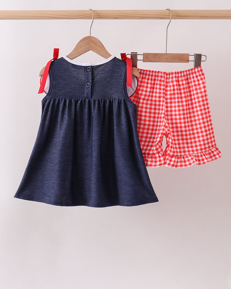Navy denim ruffle dress with button placket and red bow straps, paired with gingham shorts