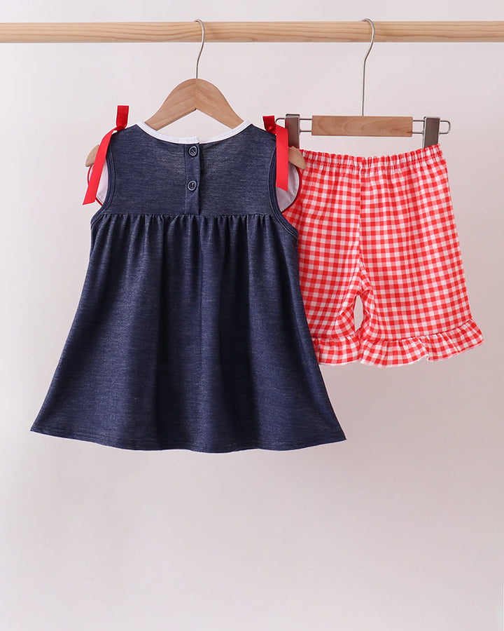 Navy denim ruffle dress with button placket and red bow straps, paired with gingham shorts