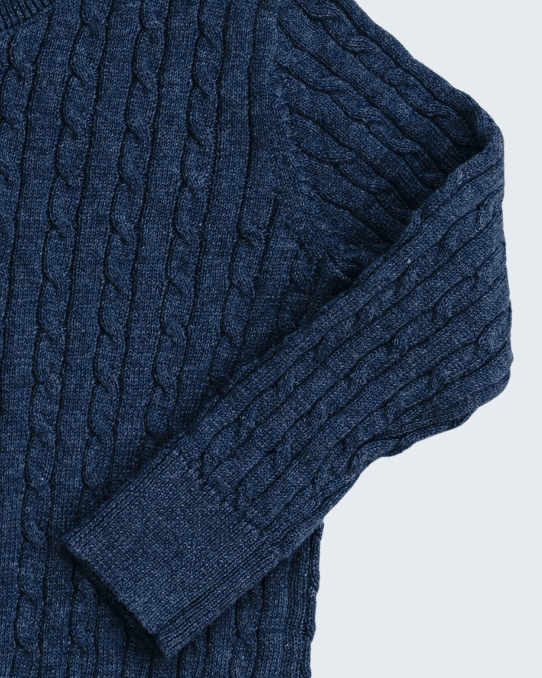 Close-up of a navy blue cable-knit sweater showing the detailed knit texture and ribbed cuff.